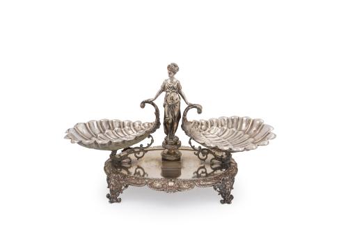 107   -  <p><span class="object_title">MENESES<br/>Espectacular centro en plateado de Meneses, S. XIX, en forma de figura femenina con corona laureada apoyada en dos grandes veneras. Sobre base oval con decoración perimetral relevada de elementos vegetales y espejuelos, soportada por patas de mascarones. </span><br></p>