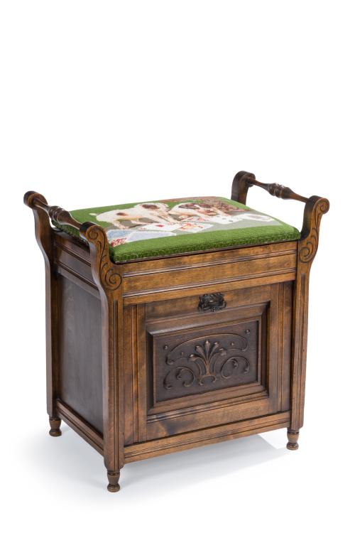 399 - <p><span class="object_title">Mueble revistero en madera tallada. S. XX.<br/>Parte superior con tapa abatible y compartimento al interior, decorada con escena de perritos jugando a las cartas en "petit point". Frente también abatible con puerta e interior compatimentado. </span><br></p>