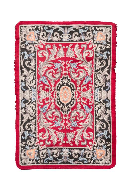 99 - <p><span class="object_title">Alfombra en lana de nudo español sobre campo rojo con decoración de roleos vegetales en tonos grises y azules, óvalo central y cenefa en negro con cestos de flores y motivos vegetales. Alguna falta.<br/><br/></span><br></p>
