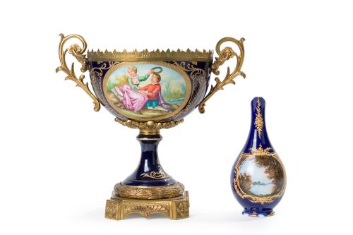 272 - <p><span class="object_title">Lote de dos piezas en porcelana de estilo Sèvres en azul cobalto con detalles en dorado y escenas esmaltadas: centro en forma de copa con montura en bronce dorado y pequeño violetero con base en bronce dorado.</span><br></p>