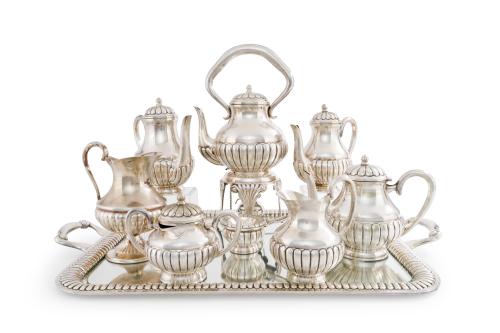 332 - <p><span class="object_title">Gran juego de café y té en alpaca con decoración gallonada formado por: samovar, tetera, 3 cafeteras, 2 jarritas, azucarero y colador. Sobre gran bandeja con asas con cristal protector. </span><br></p>