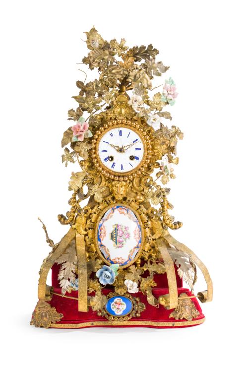 345   -  <p><span class="object_title">Reloj de sobremesa, S. XIX. <br/>En metal dorado con aplicaciones de flores, placas en porcelana y hojas recortadas. Sobre peana en terciopelo rojo. Mecanismo cuerda a llave.  Con llave. </span><br></p>
