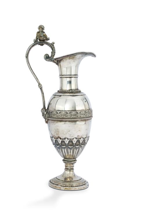 276 - <p><span class="object_title">Jarra para agua en plata española con decoración de estilo Imperio con frisos de palmetas y contarios de perlas. Gran asa rematada por mascarón y figura de amorcillo en bulto redondo. </span><br></p>