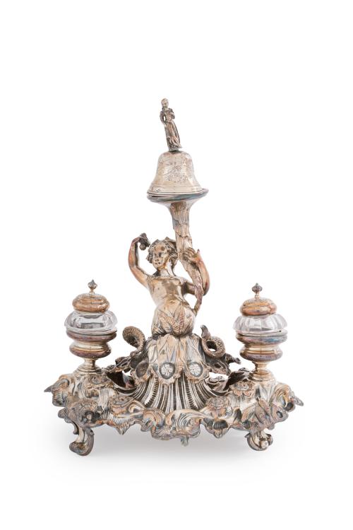 148 - <p><span class="object_title">ALPHONSE DEBAIN-FRANCIA, C.1900.<br/>Escribanía francesa en plata francesa punzonada. Fuste de tritón sujetando campanilla. Doble tintero con recipiente en cristal.<br/></span><br></p>