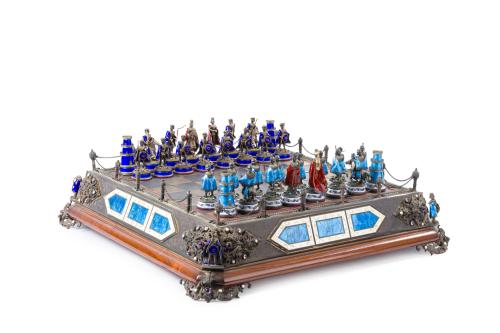 221   -  <p><span class="object_title">Importante juego de ajedrez en esmalte y plata que pertenecio a Luis II de Baviera(1845-1886), Austria o Baviera, s. XIX<br/>La caja de ajedrez es de plata dorada y el tablero esta planteado como un coso de justas, con el campo del ajedrez rodeado de seis columnitas encadenadas, guardándolas cuatro esquinas, dejando cuatro espacios de apertura centrales. Además, la caja viene orlada en sus cuatro esquinas por medallones con incrustaciones de amatista y perlas con cuatro caballeros con manto de esmalte armados de lanzas. Lleva en cada lado tres placas de esmalte con escenas de batallas y herláldicas, siendo las centrales de esmalte azul enmarcadas por esmalte blanco con orla de flores de lis y lambrequines. <br/>Cada una de las figuras esta realizada en plata sobre un pedestal con incrustaciones de piedras y perlitas, con mantos de esmalte de dos colores azul celeste y azul cobalto, salvo las del rey y la reina que llevan en los dos ejércitos mantos de esmalte que emula la púrpura real. </span><br></p>
