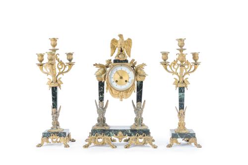 247   -  <p><span class="object_title">Guarnición de reloj de sobremesa y pareja de candelabros estilo Imperio, Francia s. XIX<br/>En bronce dorado y mármol veteado en verde. <br/>Reloj coronado por águila imperial, esfera suspendida y flanqueada por columnas que descansan en un plinto sobre el que se apoyan dos esfinges aladas sentadas. Esfera en porcelana esmaltada con numeración romana y agujas caladas doradas. Maquinaria Paris. Apoya sobre patas en forma de volutas<br/>Candelabros de 4 brazos de luz de formas vegetales, fuste a modo de columna y esfinge alada sobre base cuadrangular. Apoya sobre patas en forma de volutas. </span><br></p>