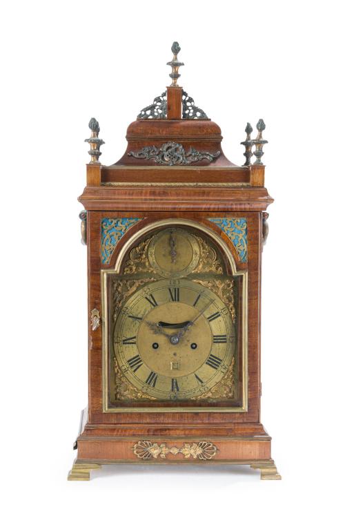 49   -  <p><span class="object_title">Reloj bracket de sobremesa Jorge III, Inglaterra, c. 1780-1790.<br/>En madera de palma de caoba, esfera en latón cincelado y aplicaciones de bronce dorado y calado. <br/>Caja cuadrangular rematada por un copete tipo "bell top" coronada por copete central y falnqueado por 4 remates de piña<br/>Esfera con numeración romana para las horas y arábiga para los minutos, con dos esferas subsidiarias en la parte superior. Las enjutas y las esquinas superiores en bronce dorado con decoración de "c" y tornapuntas vegetales. </span><br></p>